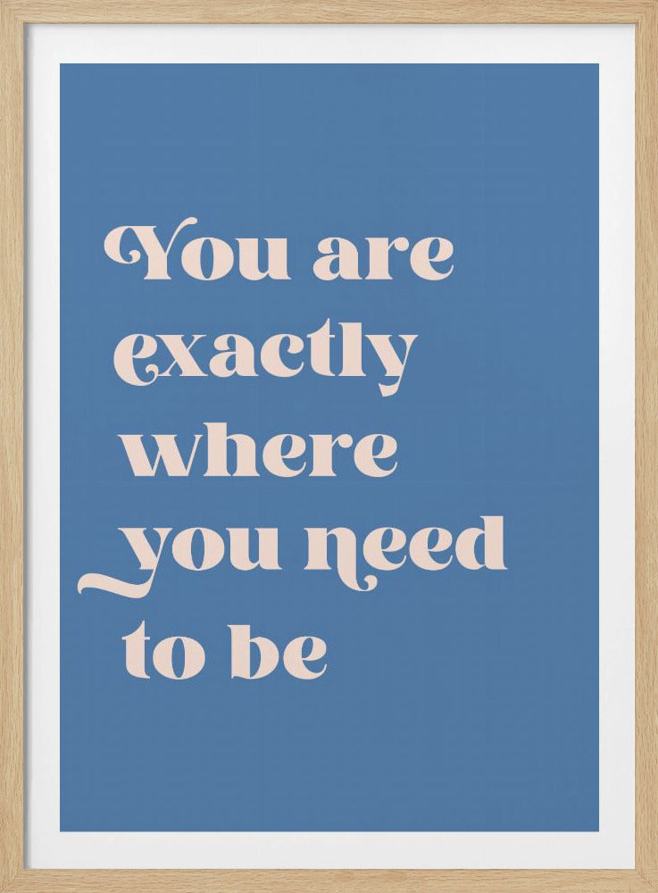 A motivational poster with the quote 'You are exactly where you need to be' written in a light beige, elegant serif font against a solid cornflower blue background, enclosed in a thin black frame. Artwork