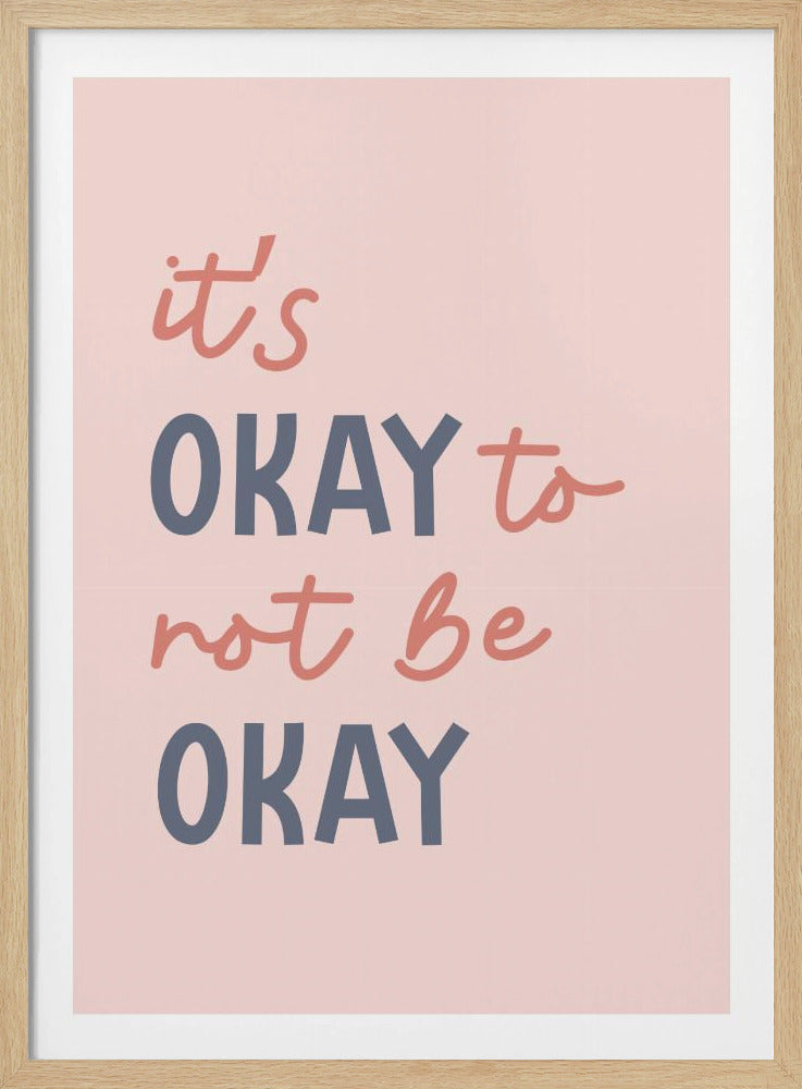 A framed art print with a light pink background featuring the quote 'it's OKAY to not be OKAY'. The text alternates between a coral pink script font and a dusty blue sans-serif font, creating a modern and supportive piece of wall art. Artwork