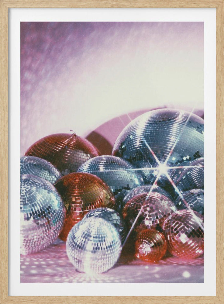 A close-up, glamorous shot of a pile of disco balls in various sizes. The balls are in shades of silver, red, and pink, reflecting a soft, sparkly pink light. A bright starburst flare shines from one of the larger silver disco balls, adding to the retro party atmosphere. Print