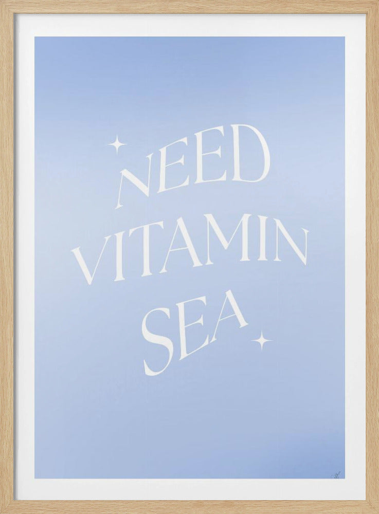 A framed poster with a light blue background featuring the phrase 'NEED VITAMIN SEA' in a wavy, white serif font, accented with small sparkles. The poster has a simple black frame. Decor