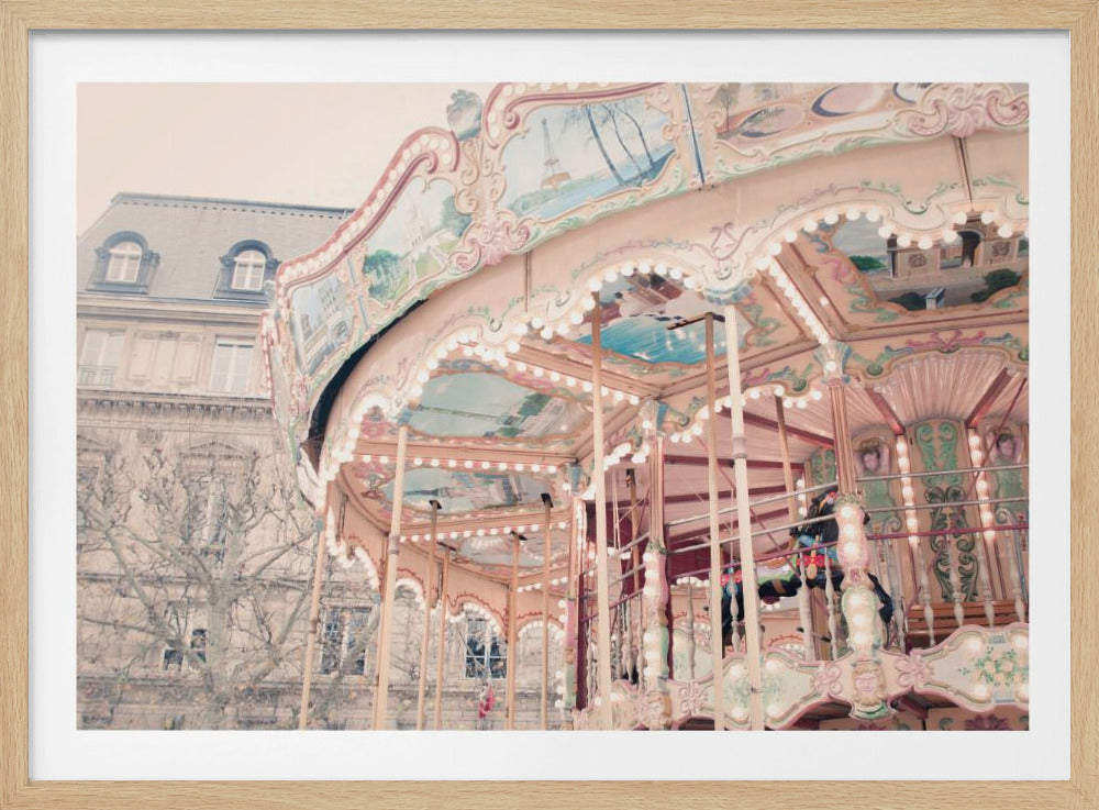 A vintage-style, soft-focus photograph of a beautiful pink and cream carousel with ornate details and lights. Paintings of Parisian scenes, including the Eiffel Tower, decorate the canopy. A classic European building stands in the background. Print