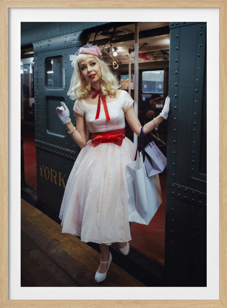 A full-length portrait of a young woman with blonde hair dressed in 1950s-style fashion, including a light pink dress with a bright red sash, a pink veiled hat, and white gloves. She smiles as she steps out of a dark, vintage train car onto a platform, holding shopping bags. Poster