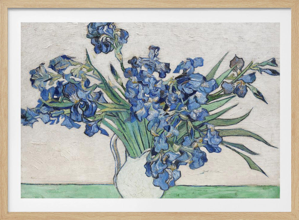 A framed print of Vincent van Gogh's famous painting 'Irises'. It features a large bouquet of vibrant blue iris flowers with long green leaves, arranged in a simple white pitcher. The background is a textured off-white wall, and the pitcher rests on a light green surface. The painting is in the post-impressionist style with thick, visible brushstrokes. Wall Art