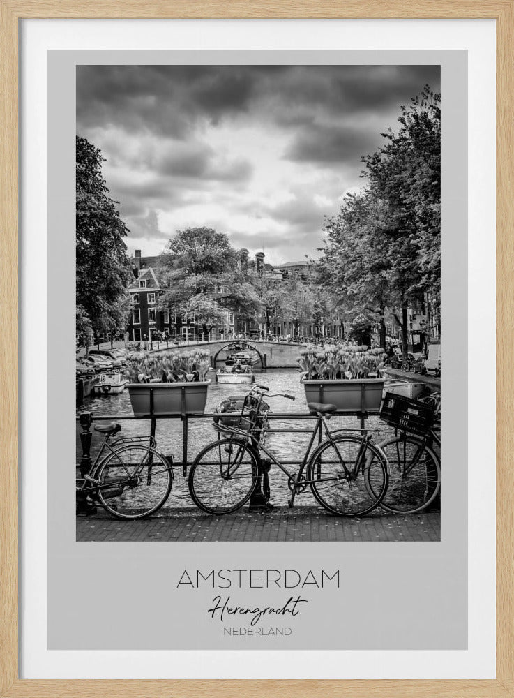 A black and white poster of the Herengracht canal in Amsterdam. In the foreground, two bicycles are parked by a railing with flower boxes. In the background, there's a classic view of the canal with a bridge, canal houses, and boats under a cloudy sky. The bottom of the poster has text that reads 'AMSTERDAM Herengracht NEDERLAND'. Decor