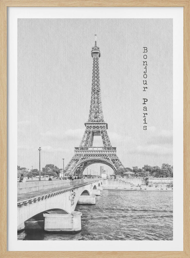 A vertical black and white framed photograph of the Eiffel Tower in Paris. The view is from across the Seine river, with a bridge leading towards the iconic landmark. On the right side of the image, the text 'Bonjour Paris' is written vertically in a typewriter font. Print