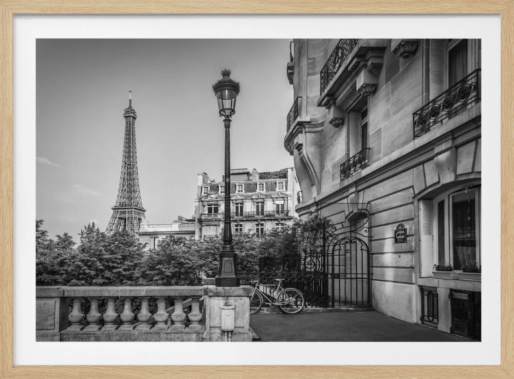 A classic black and white photograph of a Parisian street scene, framed in silver. The Eiffel Tower is visible in the distance, with a traditional lamppost, an elegant stone building with balconies, and a bicycle in the foreground. Wall Art