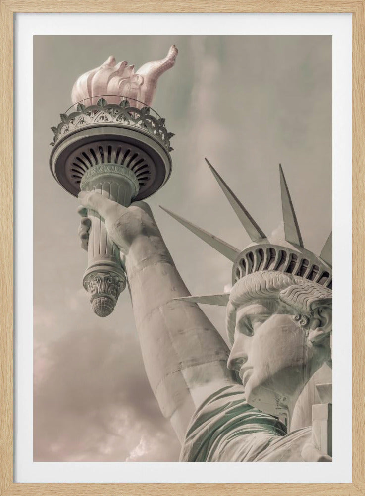 A low-angle, close-up photograph of the Statue of Liberty with a vintage color treatment. The shot captures her profile, crown, and her arm holding the torch aloft against a muted, cloudy sky, all enclosed in a thin black frame. Poster
