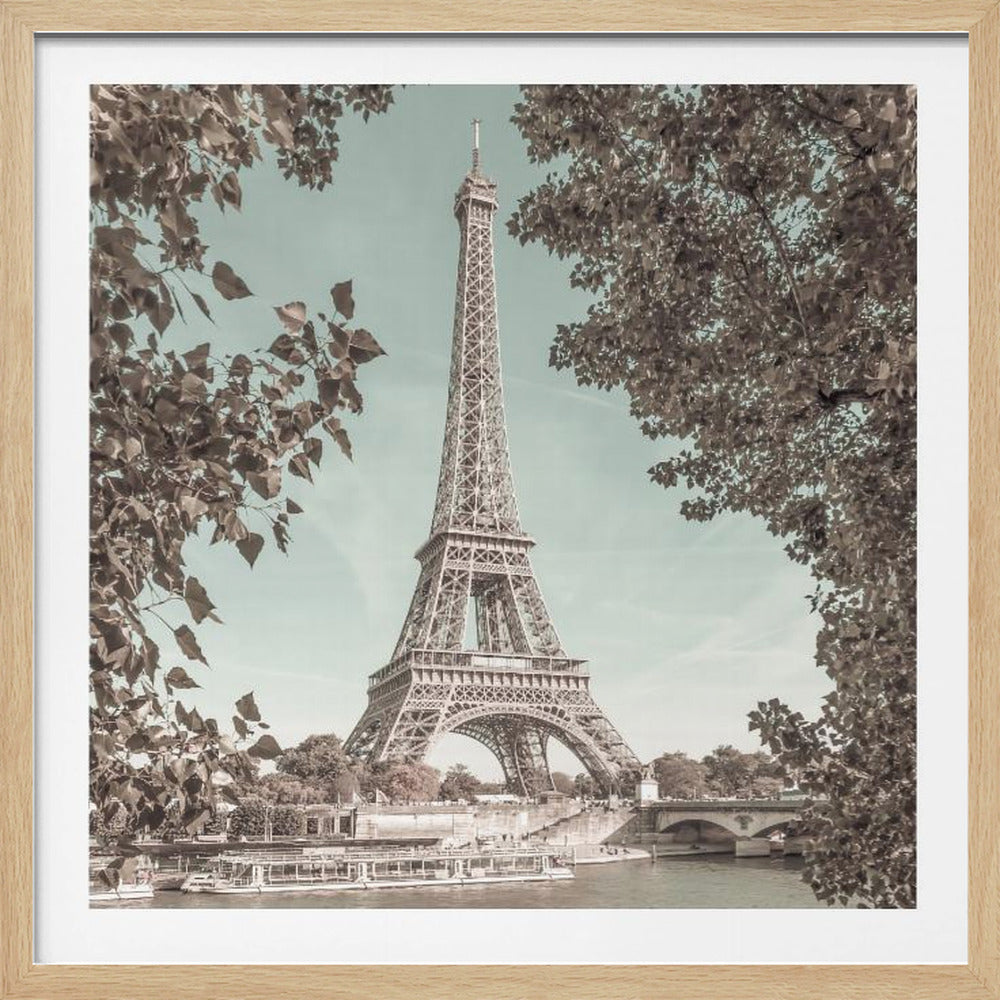 A vintage-style photograph of the Eiffel Tower in Paris, framed by sepia-toned tree branches. The tower stands tall against a muted teal sky, with tour boats visible on the Seine River below. Poster