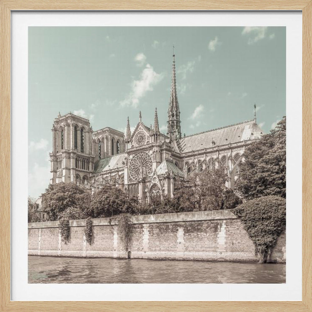 A vintage-style photograph of the Notre-Dame Cathedral in Paris, presented in a light wood frame. The view is from across the Seine River, with the cathedral's intricate gothic architecture rendered in sepia tones against a pale teal sky. Print