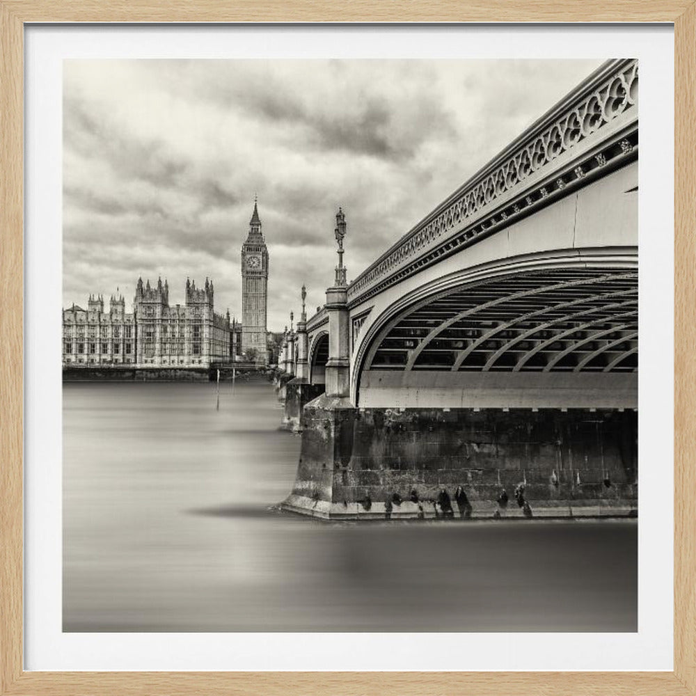A framed, long-exposure, black and white photograph of London. The image shows Westminster Bridge from a low angle on the right, with the River Thames appearing smooth and misty. In the background on the left are the Houses of Parliament and the Big Ben clock tower under a cloudy sky. Wall Art