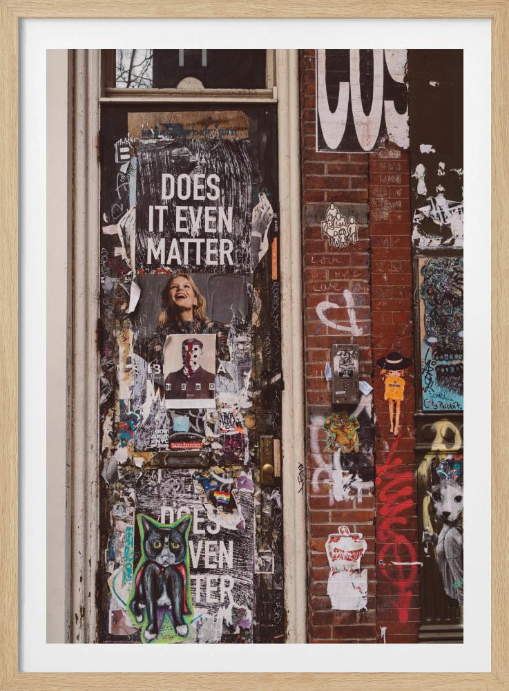 A close-up of a weathered dark door and an adjacent brick wall, both covered in a dense collage of street art, including peeling posters, stickers, and graffiti. A prominent poster on the door asks 'DOES IT EVEN MATTER' in bold white letters. Wall Art