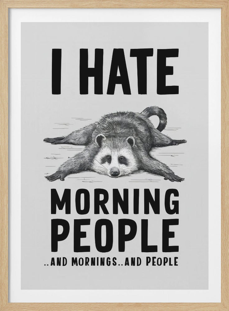 A humorous black and white framed print featuring a tired-looking raccoon lying flat on its stomach. Above the raccoon, bold text reads 'I HATE', and below it, 'MORNING PEOPLE'. A smaller line at the very bottom adds '..AND MORNINGS..AND PEOPLE'. Print