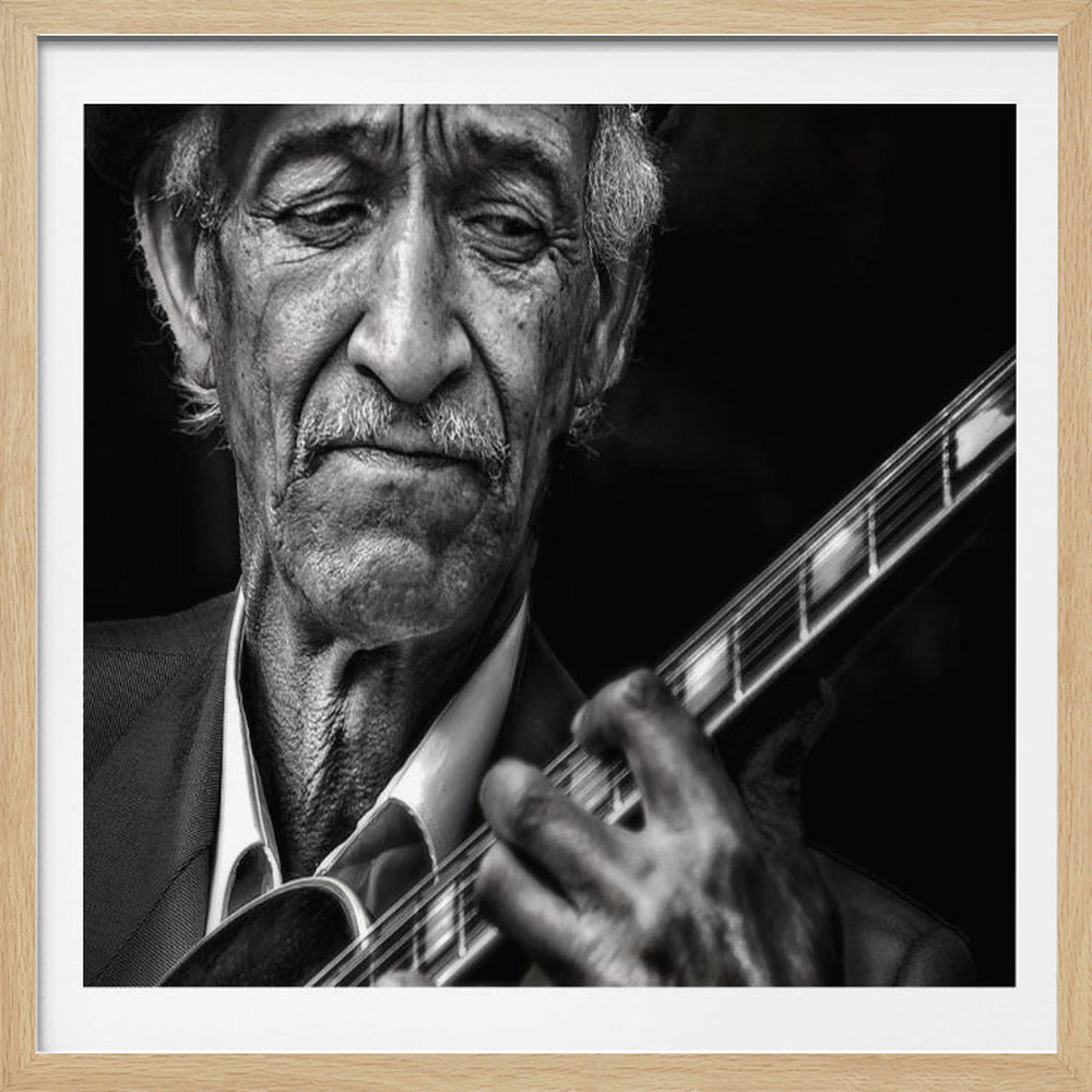 A close-up, black and white framed portrait of an elderly musician wearing a beret. His face is weathered and expressive as he looks down at the stringed instrument he is playing, his hands positioned on the fretboard. Decor