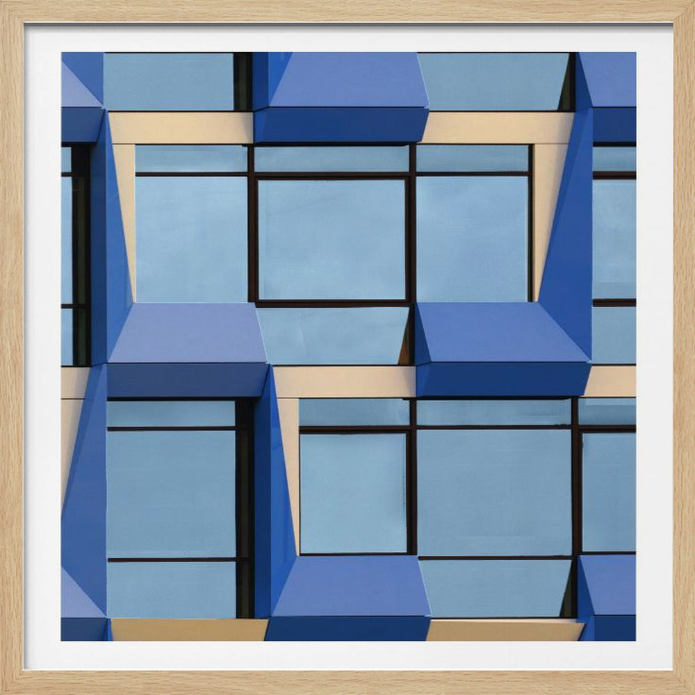 A framed abstract architectural photograph showing a repeating pattern of a modern building's facade. The image features geometric, three-dimensional blue elements surrounding light blue windows with black frames, all set against horizontal cream-colored bands. The entire piece is presented within a light wood frame. Print