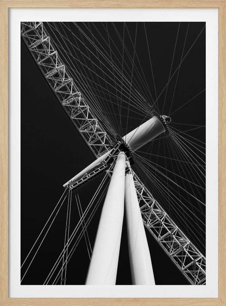 A dramatic low-angle, black and white photograph of a large Ferris wheel, focusing on the central hub and supporting structure. The image captures the white A-frame legs and the intricate lattice of the wheel's rim, with numerous tension cables radiating outwards against a solid black sky, creating a strong sense of perspective and geometric pattern. Artwork