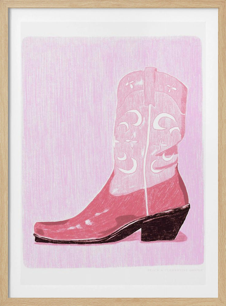 A framed art print of a pink cowboy boot against a light pink, textured background. The boot is illustrated in a block-print style with shades of pink, white decorative inlay patterns of moons and stars, and a dark brown heel and sole. Decor