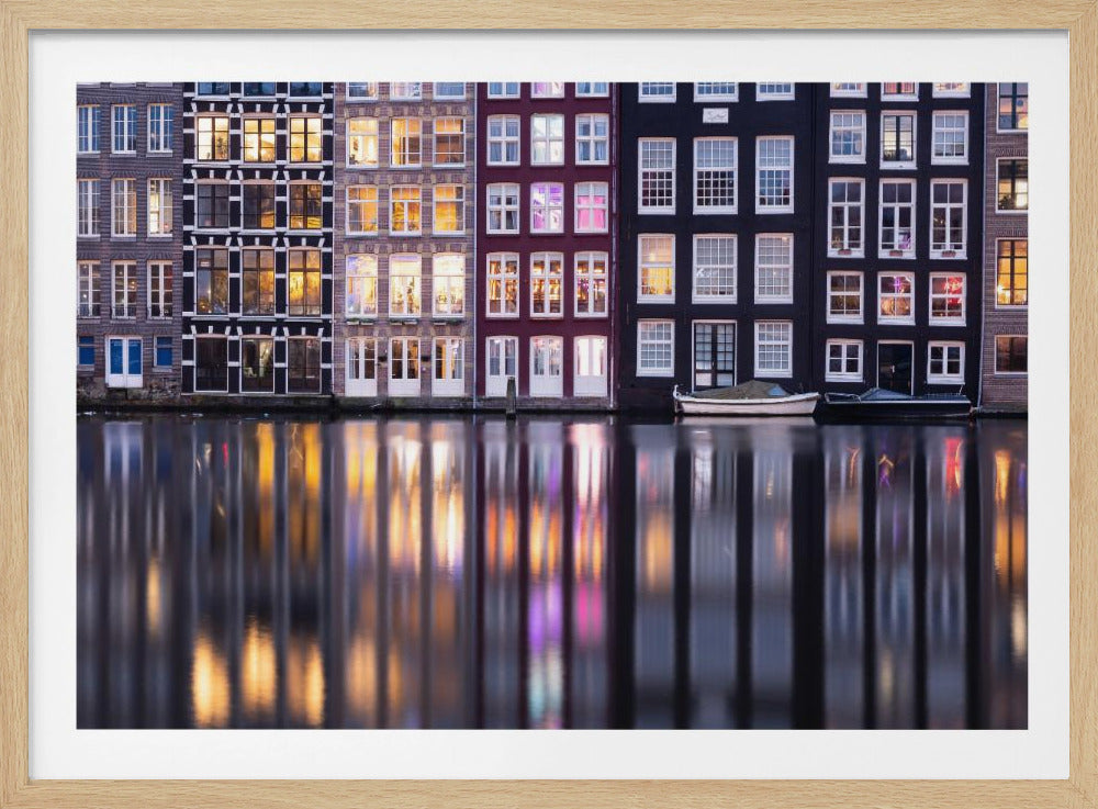 A framed photograph of colorful Amsterdam canal houses at night, their illuminated windows casting vibrant, shimmering reflections on the water below. Artwork