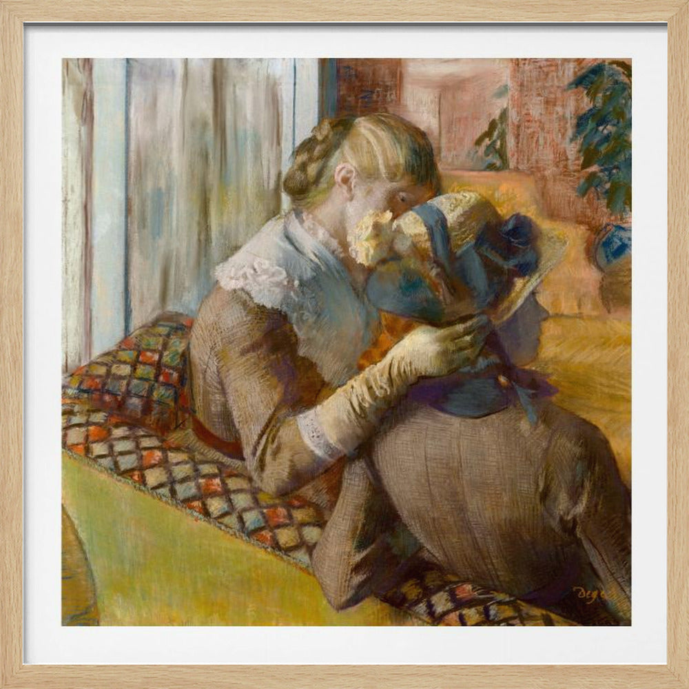 A framed Impressionist painting by Edgar Degas depicting two women. One woman, with blonde hair tied back, adjusts a hat with a blue ribbon on the other woman who is sitting with her back mostly to the viewer on a colorful patterned sofa. Print