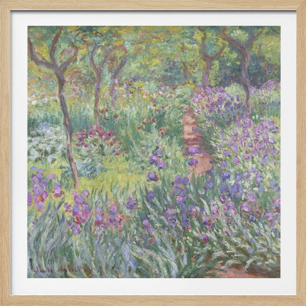 An impressionist painting by Claude Monet, 'The Artist's Garden at Giverny,' set in a light wood frame. The artwork depicts a lush, vibrant garden with a path winding through it. The foreground is dominated by purple irises and tall green leaves, while the background features trees and a mix of colorful flowers in shades of red, yellow, and white, all rendered with visible, textured brushstrokes. Print