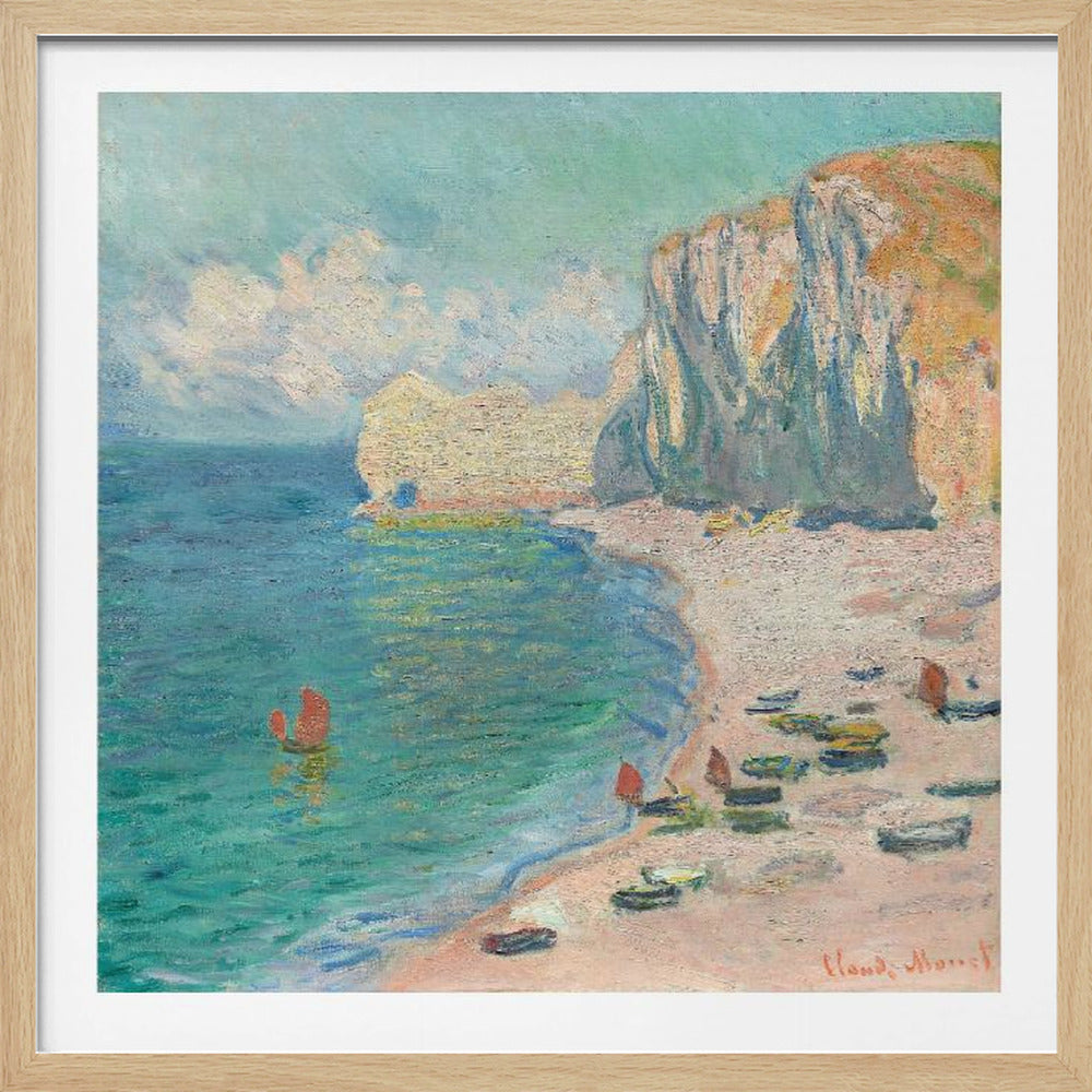 An impressionist painting by Claude Monet depicting the beach at Étretat, France, enclosed in a light wood frame. The artwork shows tall, light-colored cliffs on the right, a sandy beach with small boats, and vibrant turquoise water with a few red-sailed boats. The sky is partly cloudy. Decor