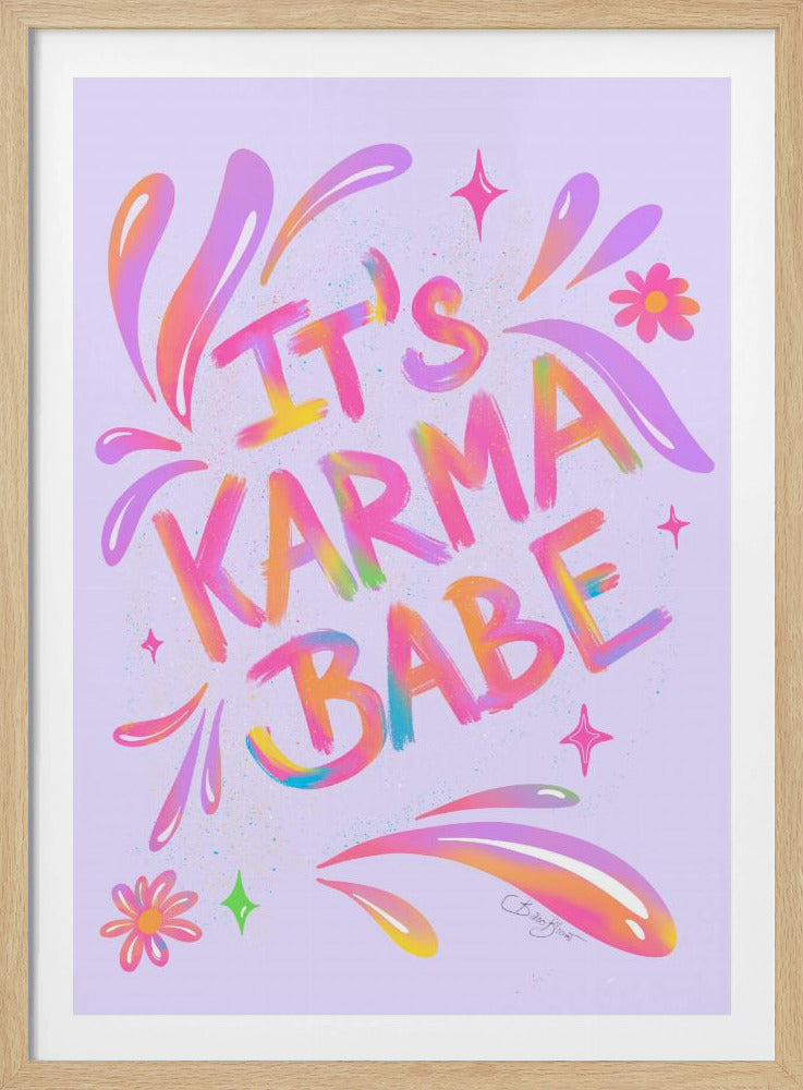 A framed art print featuring the phrase 'IT'S KARMA BABE' in a vibrant, multi-colored, graffiti-style font on a light purple background. The letters blend shades of pink, yellow, orange, and blue. The text is embellished with colorful swirls, flowers, and sparkles, creating a playful and energetic design. Decor