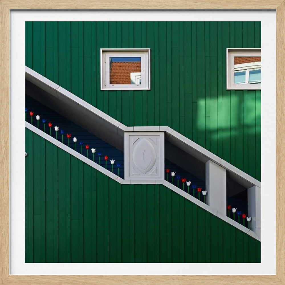 A framed photograph of a modern building with a dark green vertical-paneled facade, featuring a large, white-framed diagonal window that resembles a staircase, decorated with small red, white, and blue tulips. Two small square windows are positioned above. Decor
