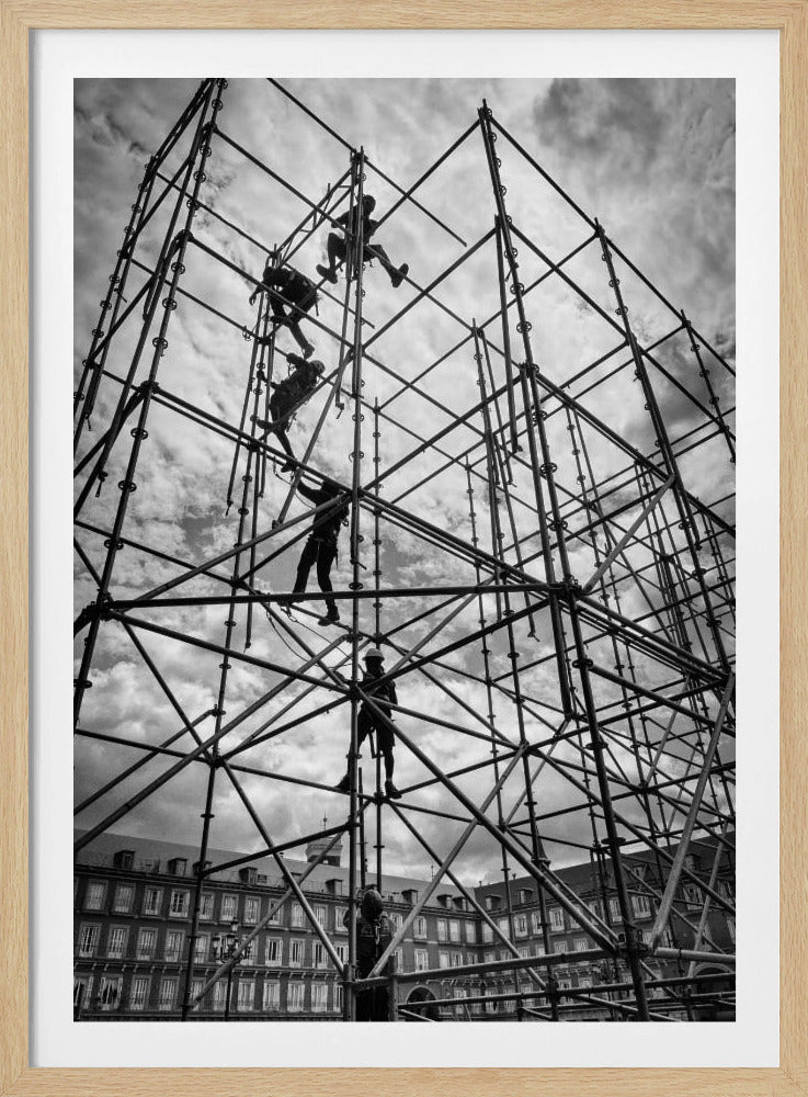 A dramatic, low-angle black and white photograph of construction workers climbing a massive, intricate metal scaffolding structure, silhouetted against a cloudy sky with a historic building in the background. Artwork