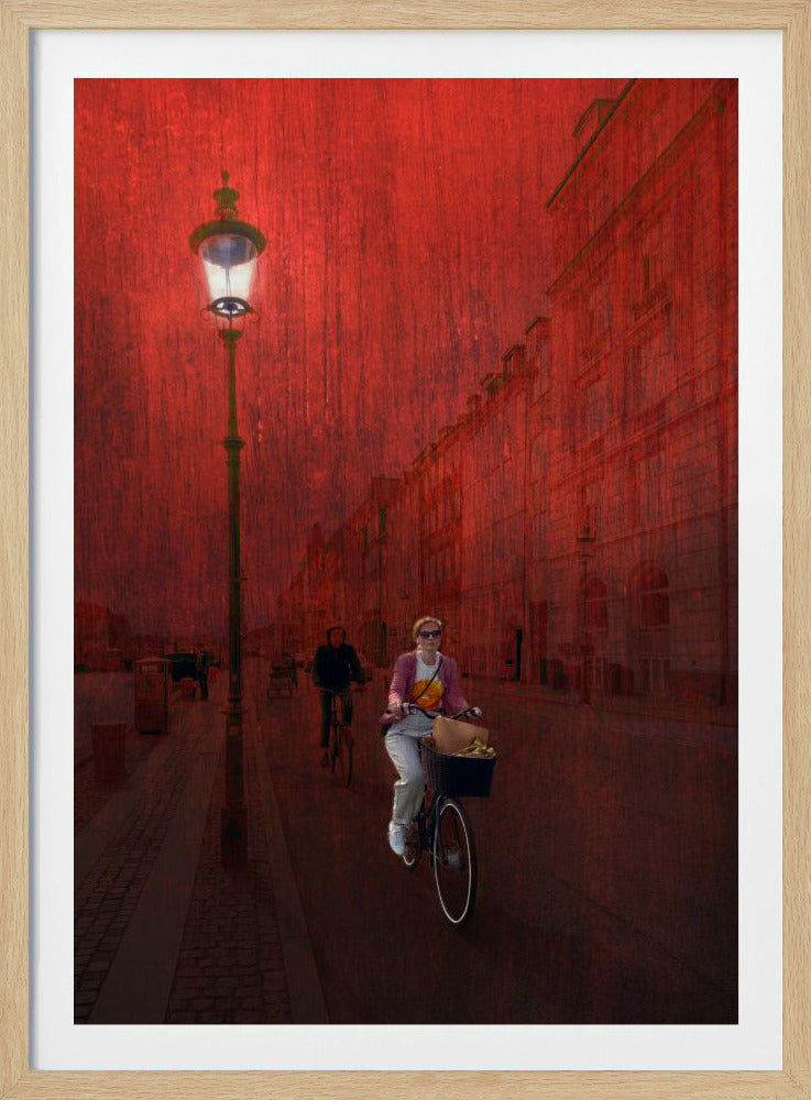 A surreal artistic image of a city street bathed in a textured red light. A woman rides a bicycle with a basket towards the viewer, while another cyclist is in the background. A tall, ornate lamppost is lit on the left side of the cobblestone street. Wall Art