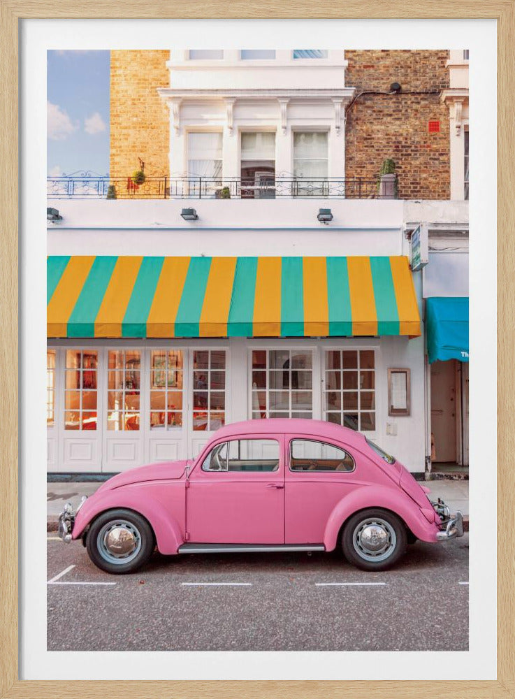 A vibrant, eye-level photograph of a vintage pink Volkswagen Beetle parked on a city street in front of a charming white storefront with a bold yellow and teal striped awning. Wall Art