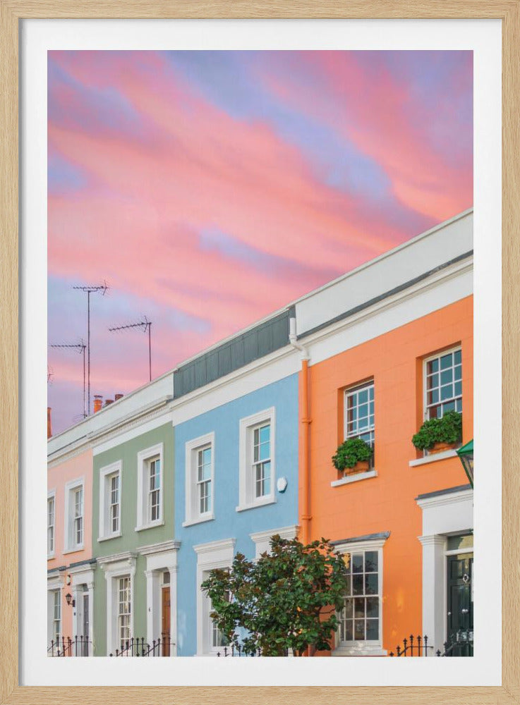 A row of colorful pastel townhouses in shades of orange, blue, green, and pink, viewed from a low angle against a dramatic, cloudy pink and purple sunset sky. Poster