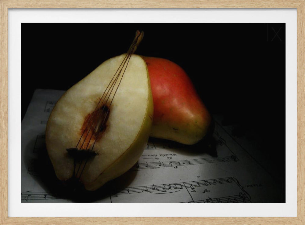A creative still life photo of a pear cut in half and strung like a miniature cello, resting on sheet music next to a whole red pear against a dark background. Print
