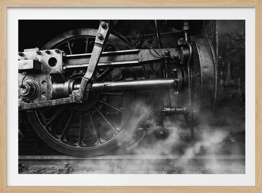 A dramatic, black and white close-up photograph of the wheels and driving rods of a steam locomotive. Puffs of steam rise from the tracks, partially obscuring the lower part of the machinery. Print