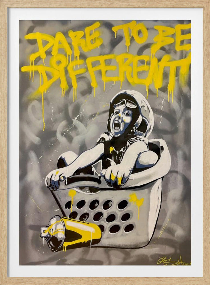 A graffiti-style painting of a child wearing a helmet and goggles, screaming with excitement while sitting inside a laundry basket. Above them, the words 'DARE TO BE DIFFERENT' are spray-painted in vibrant, dripping yellow. A yellow spray can lies beside the basket, all set against a gray, abstract background. Wall Art