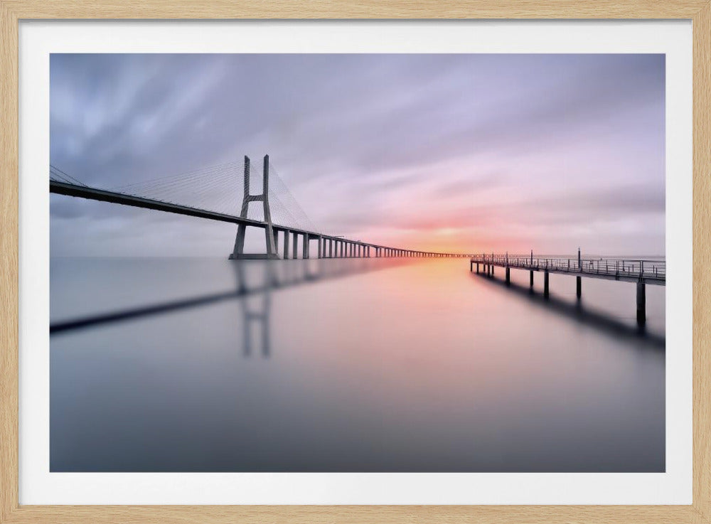A serene long-exposure photograph of a modern cable-stayed bridge and a pier stretching over mirror-like water at sunset. The sky is filled with soft, streaky clouds in hues of pink and purple, reflected on the calm water's surface, all enclosed in a silver frame. Decor