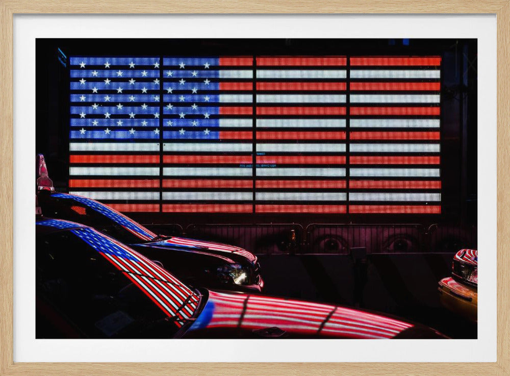 A large illuminated American flag on a billboard at night, with its red, white, and blue lights reflecting on the glossy hoods of two cars in the foreground. Wall Art
