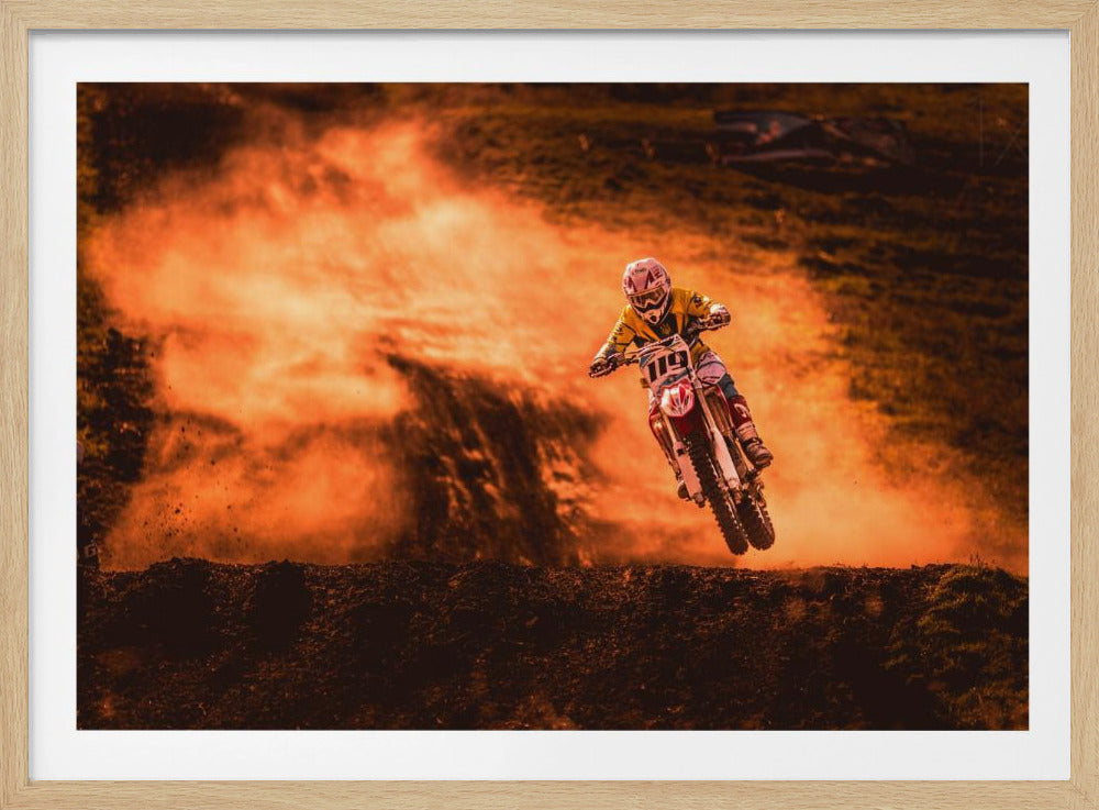 An action-packed photo of a motocross rider in mid-air, jumping their dirt bike over a mound of earth. A large cloud of orange dust billows behind them, creating a dramatic and fiery background. Wall Art