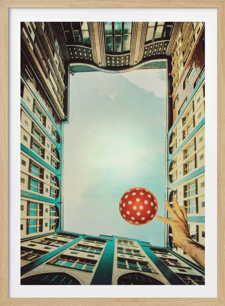 A surreal, worms-eye view looking up from a courtyard, where distorted teal and cream buildings frame a light blue sky. A hand reaches into the frame, balancing a red and white polka-dotted ball on its fingertip. Decor