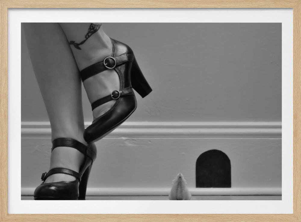 A black and white photograph showing the lower legs and feet of a woman wearing black high-heeled Mary Jane shoes. A tiny white mouse stands on its hind legs near a cartoonish mouse hole in the baseboard, looking up at the woman. Artwork