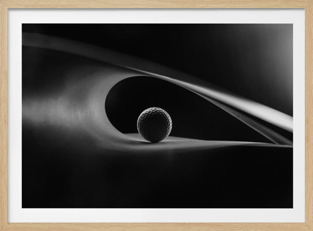 An artistic black and white photograph of a golf ball resting inside the gentle curve of a dark, abstract shape, creating a minimalist and dramatic composition with strong light and shadows. Poster
