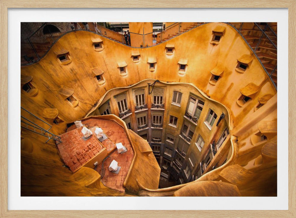 A high-angle photograph looking down into the surreal, undulating inner courtyard of an architectural masterpiece. The warm, golden-ochre walls curve organically, dotted with small, hooded windows, encircling the deep central lightwell that reveals floors of apartments below. Wall Art