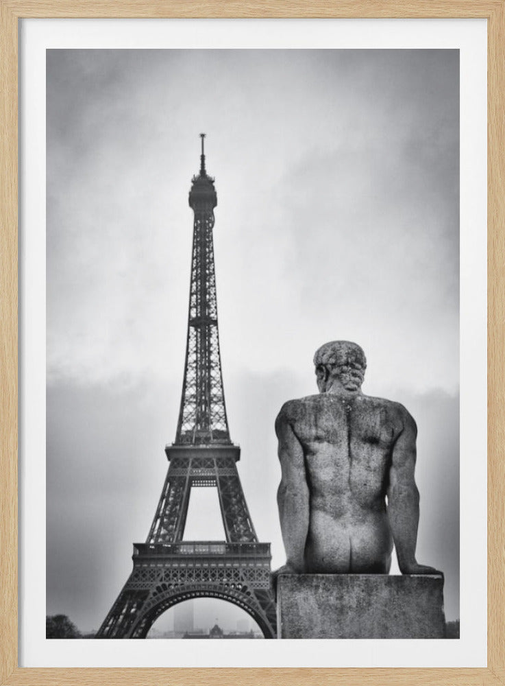 A black and white photograph capturing a contemplative scene in Paris, with the back of a seated, muscular male stone statue in the foreground looking towards the iconic Eiffel Tower which stands tall against a cloudy sky. Print