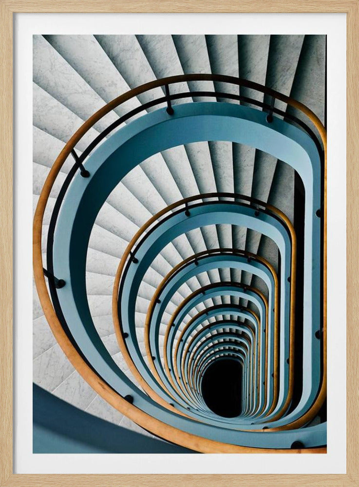 A high-angle, top-down photograph of a multi-story rectangular spiral staircase, creating a hypnotic, receding pattern. The steps are light gray marble, contrasted by shadows, and the balustrade is a striking light blue with a warm wooden handrail, leading down to a dark abyss at the center. Wall Art
