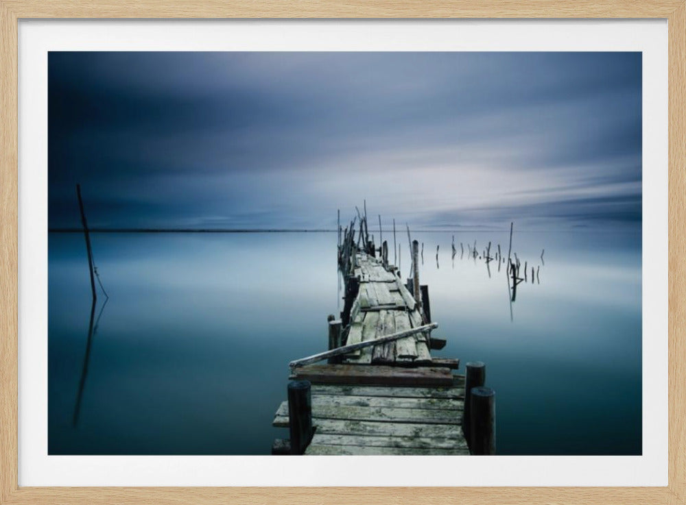 A framed, long exposure photograph of a weathered wooden pier extending into calm, misty blue water under a dramatic, cloudy sky. Wall Art