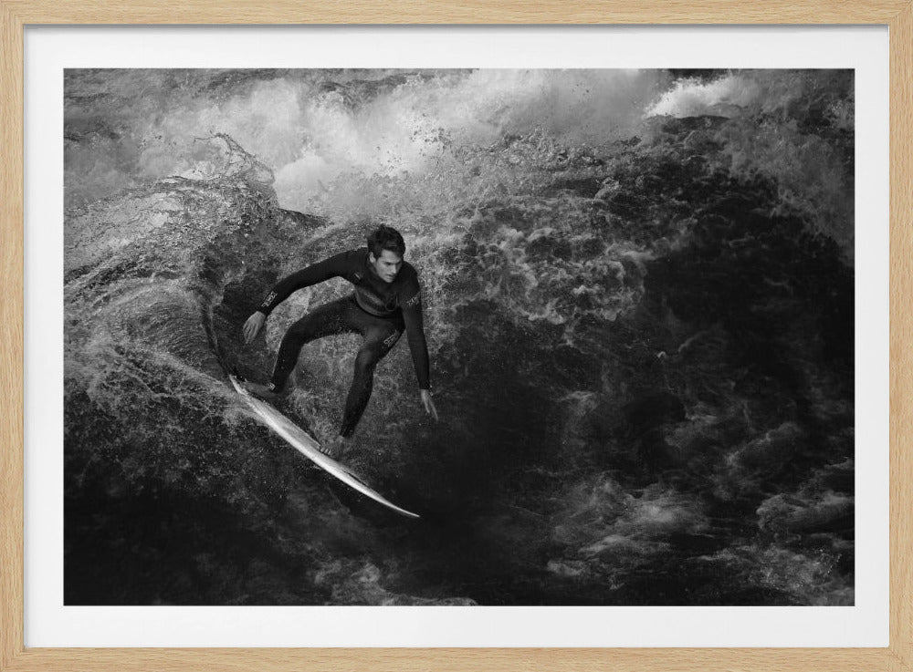 A dramatic black and white photograph of a surfer in a wetsuit skillfully riding down the face of a large, turbulent wave. The image is enclosed in a silver frame. Wall Art