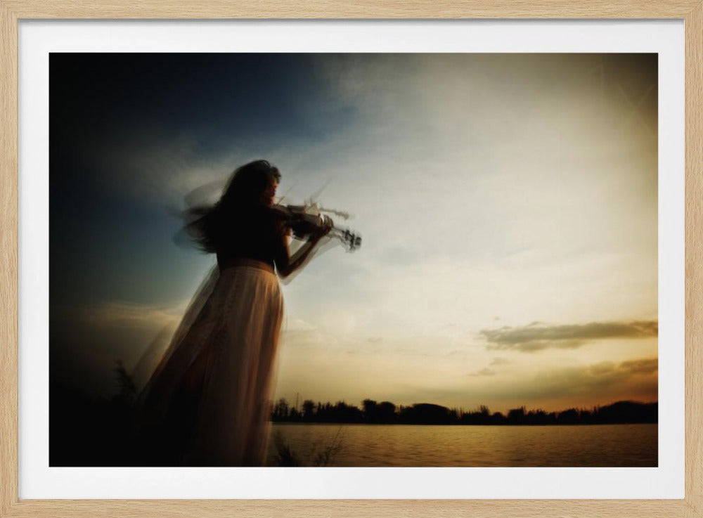 An artistic, framed photograph with motion blur capturing the silhouette of a woman in a long flowing skirt playing the violin by a lake against a dramatic sunset sky. Poster