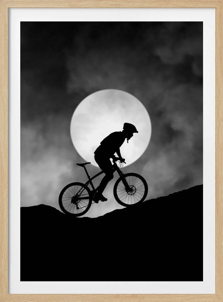 A dramatic black and white silhouette of a mountain biker riding uphill against the backdrop of a large, full moon in a cloudy night sky. Decor