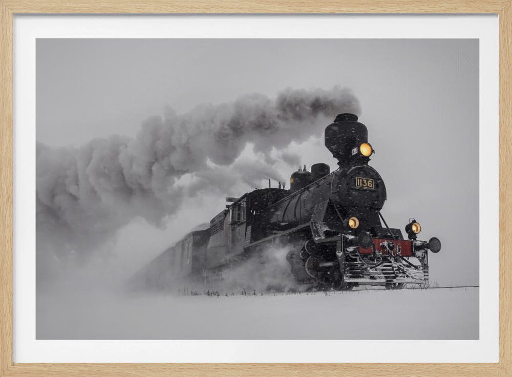 A dramatic black and white photograph of a classic steam train, number 1136, plowing through a heavy snowstorm, with its headlights glowing and a large plume of smoke trailing behind it. The image is presented within a silver frame. Print