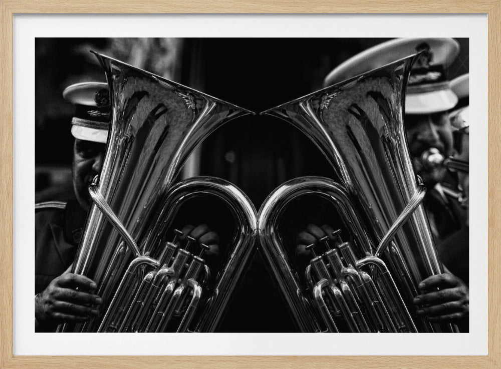 A dramatic black and white close-up photograph of two musicians holding their shiny tubas, positioned symmetrically to create a mirror image effect. The musicians are wearing uniforms and hats, and their faces are partially obscured by the large brass instruments. Print
