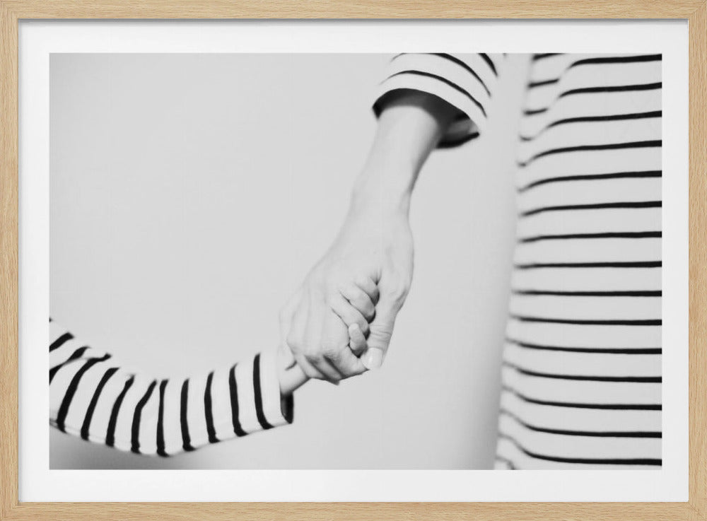 A tender black and white photograph capturing a close-up of a parent and child holding hands. Both are wearing matching striped shirts, emphasizing their connection. The image is presented in a silver frame. Print