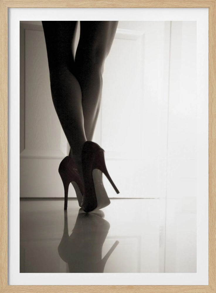 A low-angle, black and white photograph focusing on a woman's legs as she stands with them crossed. She wears dark red stiletto high heels, which cast a clear reflection on the glossy floor. Her legs are silhouetted against a bright white door in the background, creating a dramatic and sensual mood. Decor